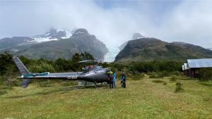 two people standing next to a helicopter in a field at Monte Balmaceda Lodge & Glaciers in Torres del Paine