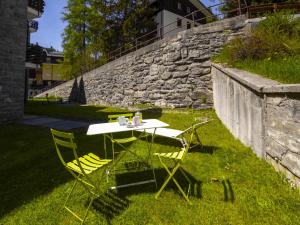 a table and chairs in the grass next to a stone wall at Studio Tigli-2 by Interhome in Madesimo