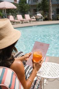 a woman sitting at a table with a book and a drink at Caravan Court Hotel in Arlington