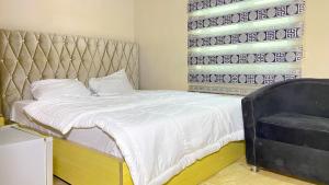 a bedroom with a bed with a padded headboard and a chair at H&Ts Bars and Hotels in Ibadan