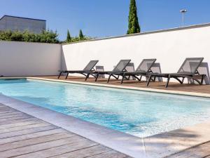 a swimming pool with lounge chairs next to a wall at ibis Carcassonne Est la Cité in Carcassonne