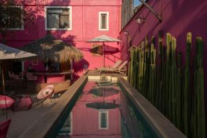a pool in front of a pink building with chairs and umbrellas at Casa Rosamate in Oaxaca City