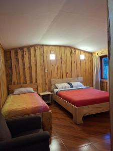 two beds in a room with wooden walls at Refugio entre Coihues in Melipeuco