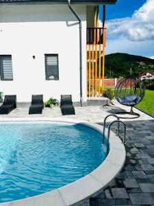 a swimming pool with a swing and a chair next to a house at CASA VIKI in Bănicel