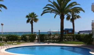 a pool with palm trees and the ocean in the background at PRIMERA LINEA DE PLAYA VILAFORTUNY in Vilafortuny