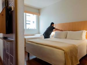 a man is standing next to a bed in a hotel room at Ibis Florianopolis in Florianópolis +171 photos