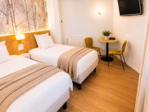 a hotel room with two beds and a table at Mercure Lourdes Impérial in Lourdes