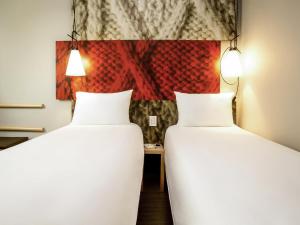 two beds in a room with a painting on the wall at Ibis Aéroport Bâle Mulhouse in Saint-Louis
