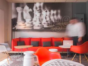 a red couch in a room with tables and chairs at ibis Dunkerque in Dunkerque