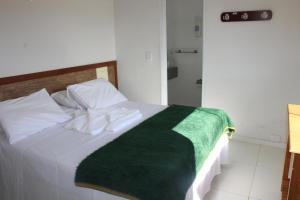 a bedroom with a white bed with a green blanket on it at Summit Capitólio Hotel in Capitólio