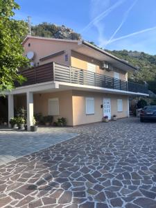 a house with a balcony and a stone driveway at Apartmani Nil in Barić Draga