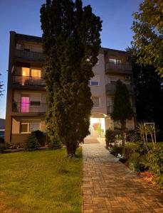 a building with a tree in front of a brick path at Ubytovanie u Tomáša in Nesvady