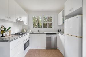 a white kitchen with white cabinets and a window at Alcheringa Cottage Amazing Location with views in Kangaroo Valley
