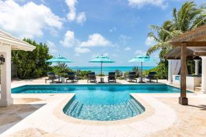 a swimming pool with chairs and umbrellas and the ocean at Villa La Percha in Providenciales