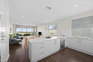 a kitchen with white cabinets and a living room at Meander - Port Noarlunga South - C21 SouthCoast Holidays in Port Noarlunga South