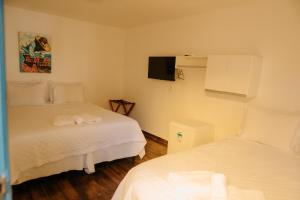 a bedroom with two beds and a tv on the wall at Pousada Areias do Pero in Cabo Frio