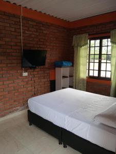 a bedroom with a bed and a tv and a brick wall at Finca Hotel Montebello in Quimbaya +25 photos