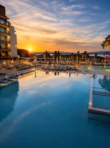 a large swimming pool with chairs and a sunset at Hotel Palms Beach Kiten in Kiten