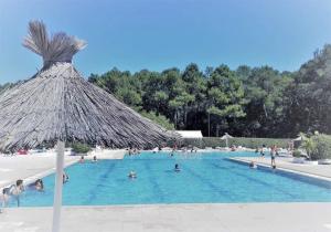 a group of people in a swimming pool with a straw umbrella at Comfortable chalet in a vacation village in Gujan-Mestras +18 photos