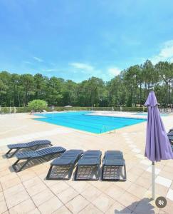 two lounge chairs and an umbrella next to a swimming pool at Comfortable chalet in a vacation village in Gujan-Mestras