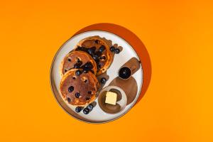 a plate of pancakes with syrup on a yellow background at Solo Society Hybrid Hotel Vilnius in Vilnius