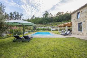a yard with a pool and two chairs and an umbrella at Casa De Pedra D'alborinhas in Arões