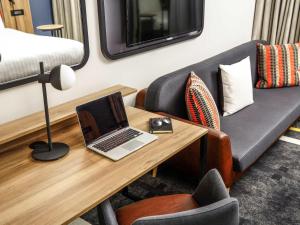 a room with a desk with a laptop and a couch at ibis Styles London Gloucester Road in London