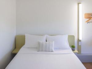 a white bed with white pillows in a room at ibis Budget Brisbane Airport in Brisbane