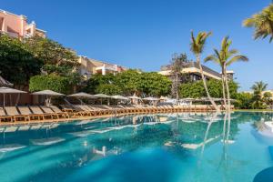 a swimming pool at a resort with chairs and palm trees at Servatur Isora Suites in Puerto de Santiago