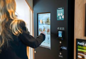 a woman is standing next to a vending machine at B&B HOTEL Magnanville in Magnanville