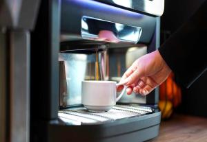 a person is holding a cup in a coffee machine at B&B HOTEL Magnanville in Magnanville