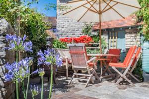a patio with chairs and an umbrella and purple flowers at Passiflora Cottage Close to Swanage Beach and Town Sleeps 7 in Swanage