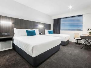 a hotel room with two beds and a desk and a window at The Sebel Canberra Civic in Canberra