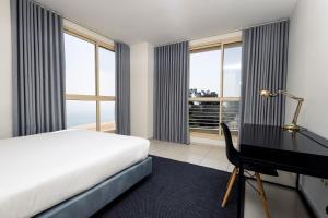 a bedroom with a bed and a desk and windows at Almar Aparthotel in Lobito