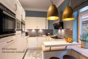 a kitchen with white cabinets and gold pendant lights at Logierhaus K15 Appartement 4 Plus in Borkum +5 photos