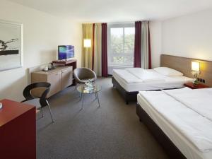 a hotel room with two beds and a desk at Mövenpick Hotel Münster am Aasee in Münster