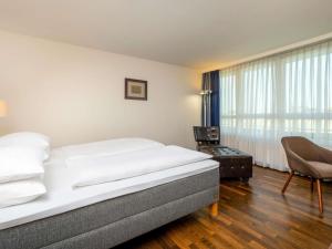 a bedroom with a bed and a chair and a window at Mövenpick Hotel Nürnberg Airport in Nuremberg +111 photos