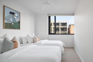 a white bedroom with two beds and a window at The Ellery in Newcastle