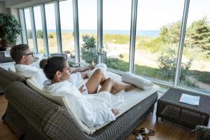 two people sitting on a couch looking at the ocean at Strandhotel Dünenmeer - Adults only in Dierhagen