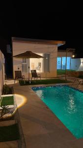 a pool at night with two chairs and an umbrella at Reef ALjabal Rest in Minthār