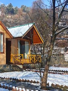 a wooden cabin with a porch in the snow at Wildwood Cabins Manali in Kulu