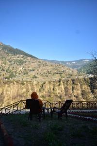 a person sitting on a chair in front of a hill at Wildwood Cabins Manali in Kulu