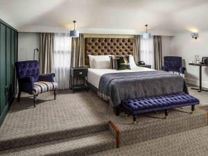 a bedroom with a large bed and two blue chairs at Mercure Oxford Hawkwell House Hotel in Oxford