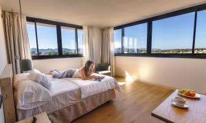 a woman laying on a bed in a room with large windows at Alcudia Boutique Apartments in Alcudia