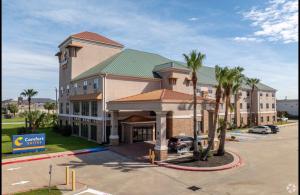 a hotel with palm trees in front of a parking lot at Comfort Suites near NASA - Clear Lake in Webster