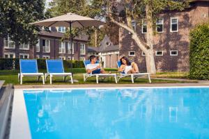 two people sitting in chairs next to a swimming pool at Hotel De Werelt Garderen in Garderen