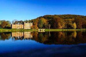 a large castle on a hill next to a lake at La Bouverie in Profondeville
