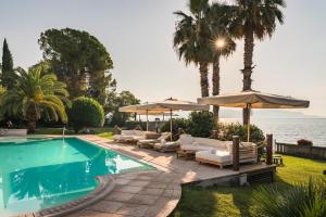 ein Swimmingpool mit Liegestühlen und Sonnenschirmen direkt am Meer in der Unterkunft Hotel Villa Capri in Gardone Riviera