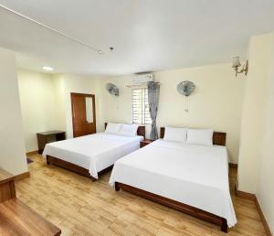 two beds in a room with white walls and wooden floors at Oriio Hotel in Cat Ba