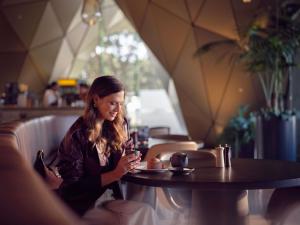 a woman sitting at a table looking at her cell phone at Pullman Auckland Airport in Auckland
